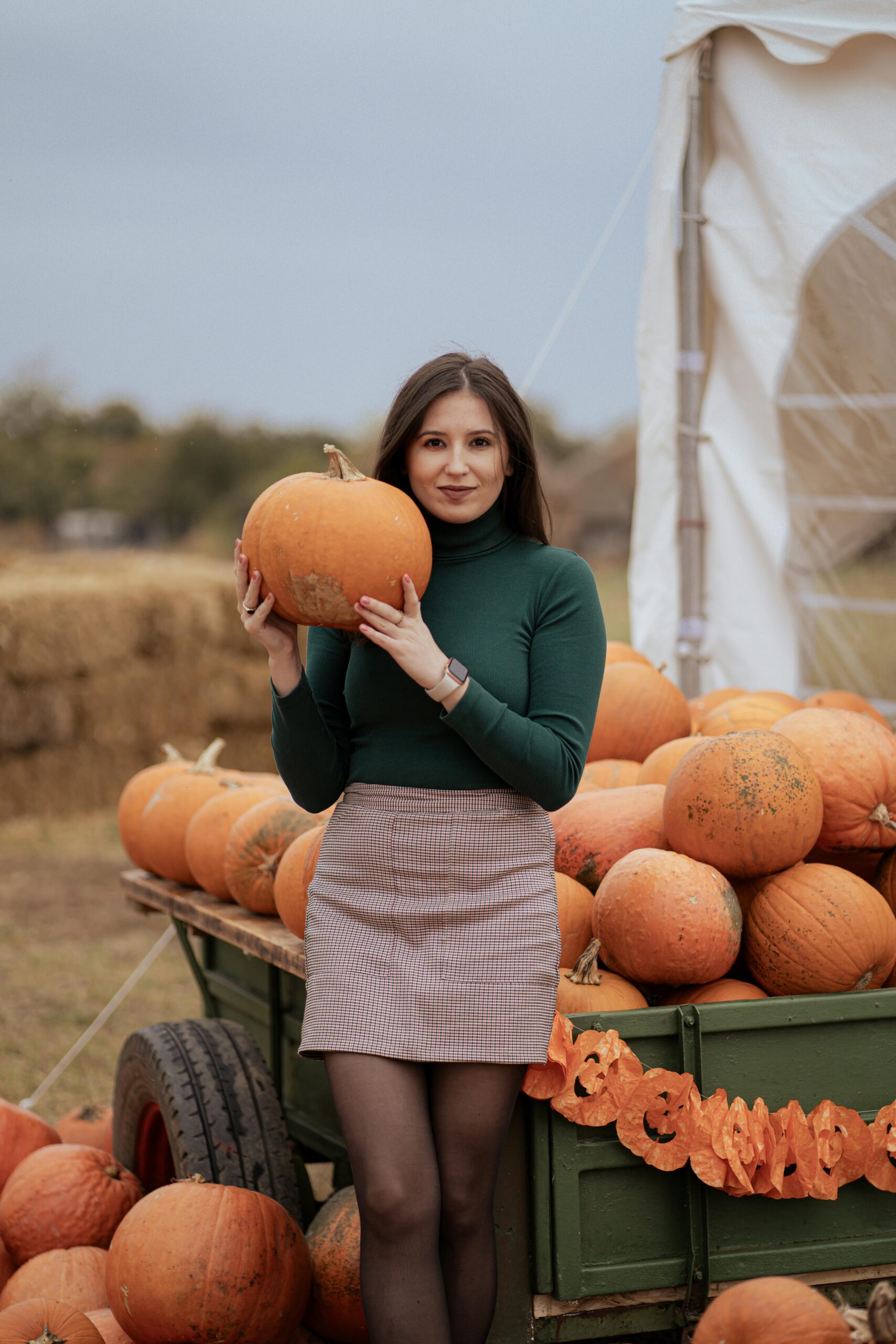 Young woman holding a pumpkin on a farm filled with pumpkins and autumn decor.